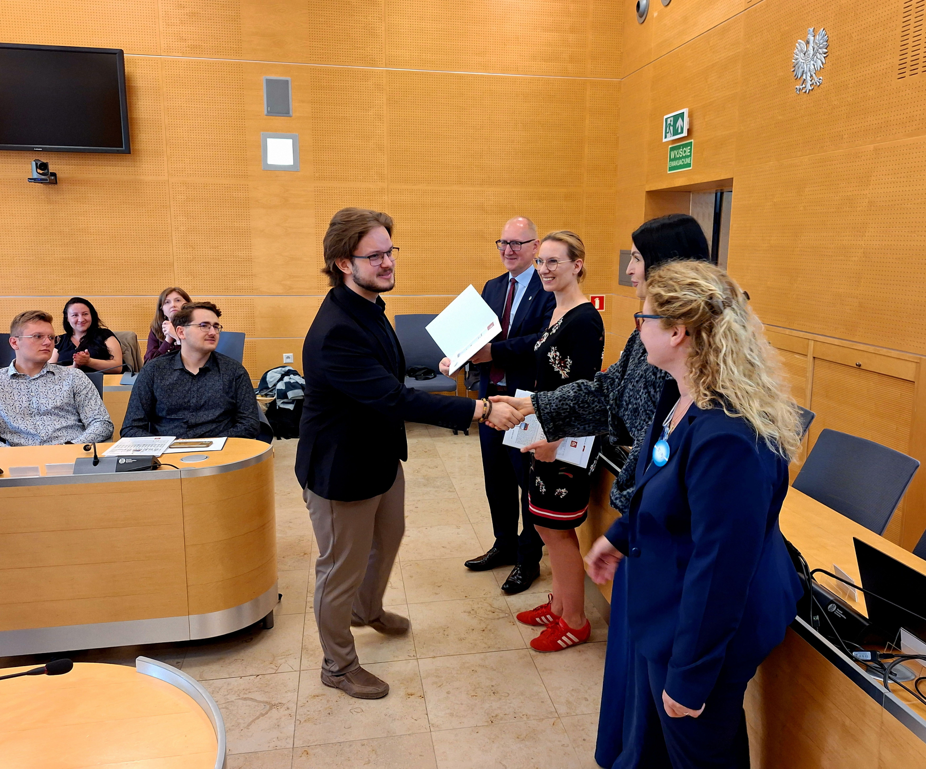 Laureat z dyplomem odbierający gratulacje od kapituły