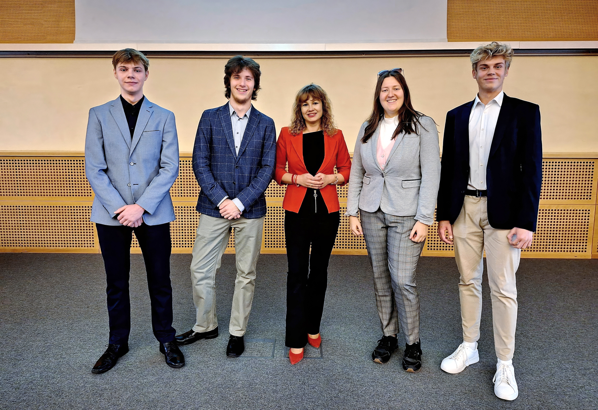 Pięć osób w eleganckich strojach stoi w rzędzie w sali wykładowej Politechniki Wrocławskiej, pozując do wspólnego zdjęcia.