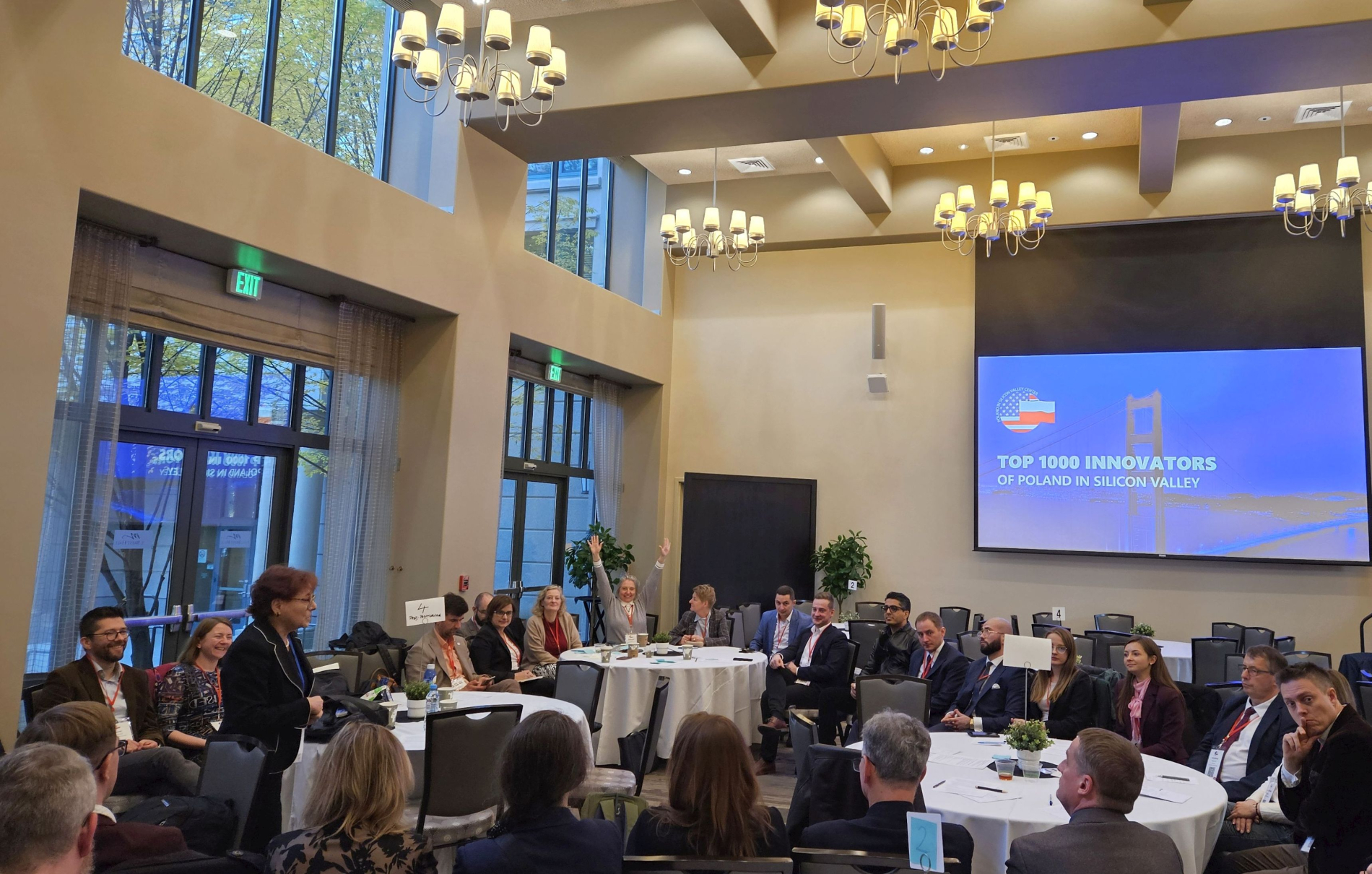 Grupa osób siedzących przy okrągłych stolikach