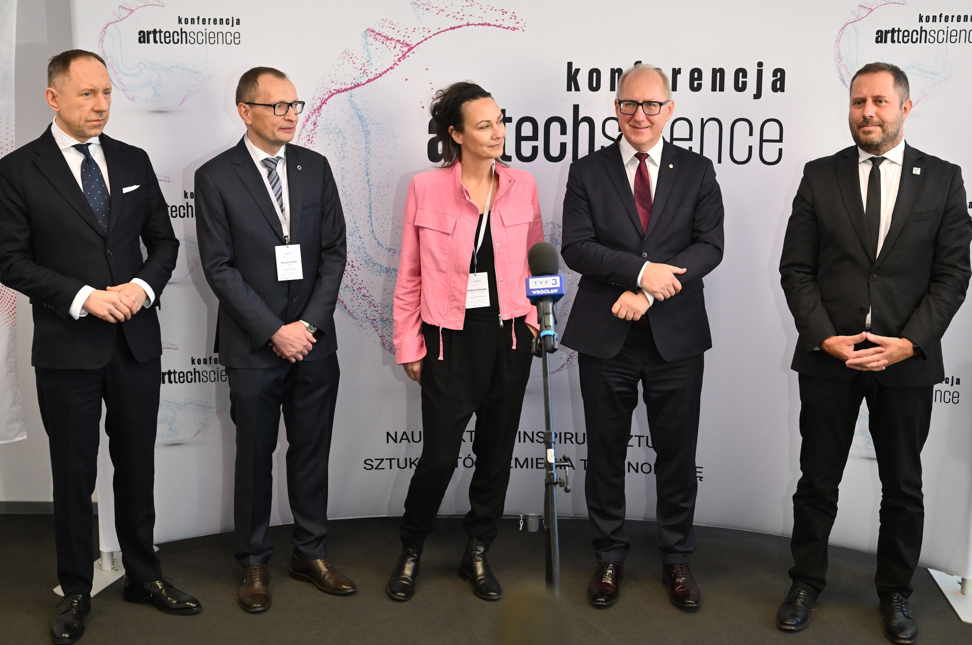 Grupa uczestników konferencji ArtTechScience pozuje przed ścianką z logo wydarzenia, przy mikrofonie z oznaczeniem TVP3 Wrocław.