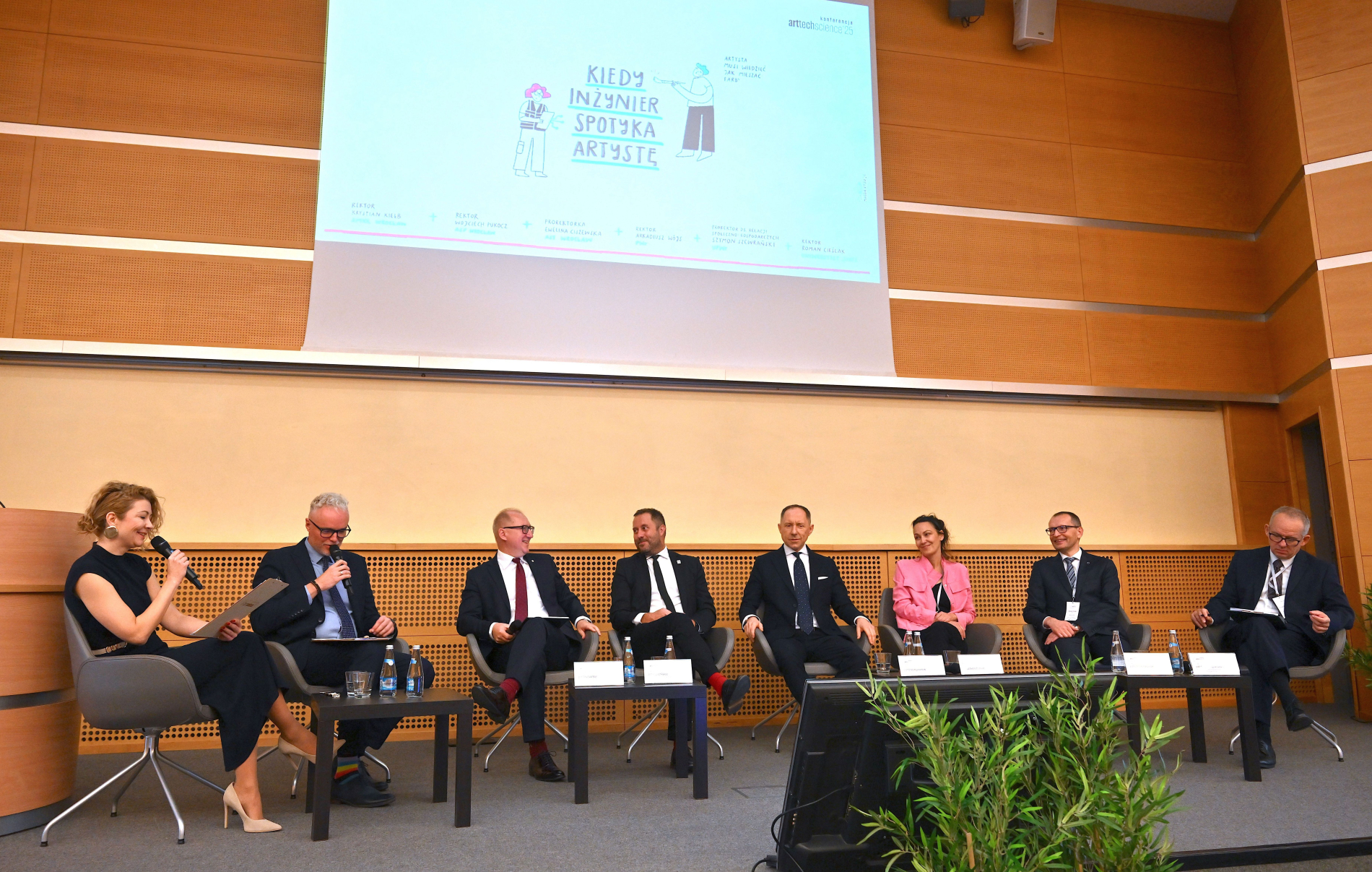 Panel dyskusyjny podczas konferencji ArtTechScience. Siedmioro uczestników rozmawia na scenie przed publicznością, pod ekranem z hasłem „Kiedy inżynier spotyka artystę”.
