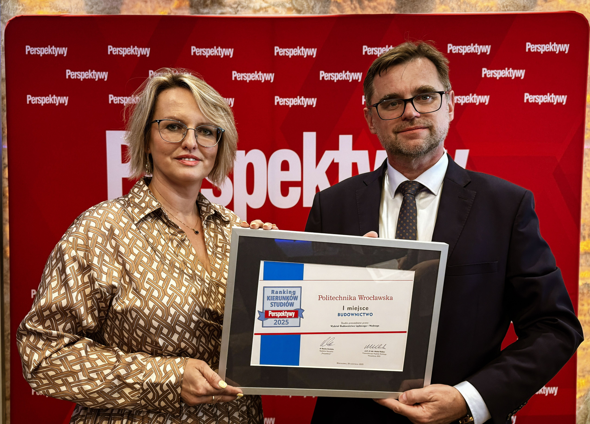 Kobieta i mężczyzna trzymają oprawiony dyplom z napisem „Politechnika Wrocławska, Ranking Kierunków Studiów Perspektywy 2025, 1 miejsce Budownictwo”. Tło stanowi ścianka z napisem „Perspektywy”.