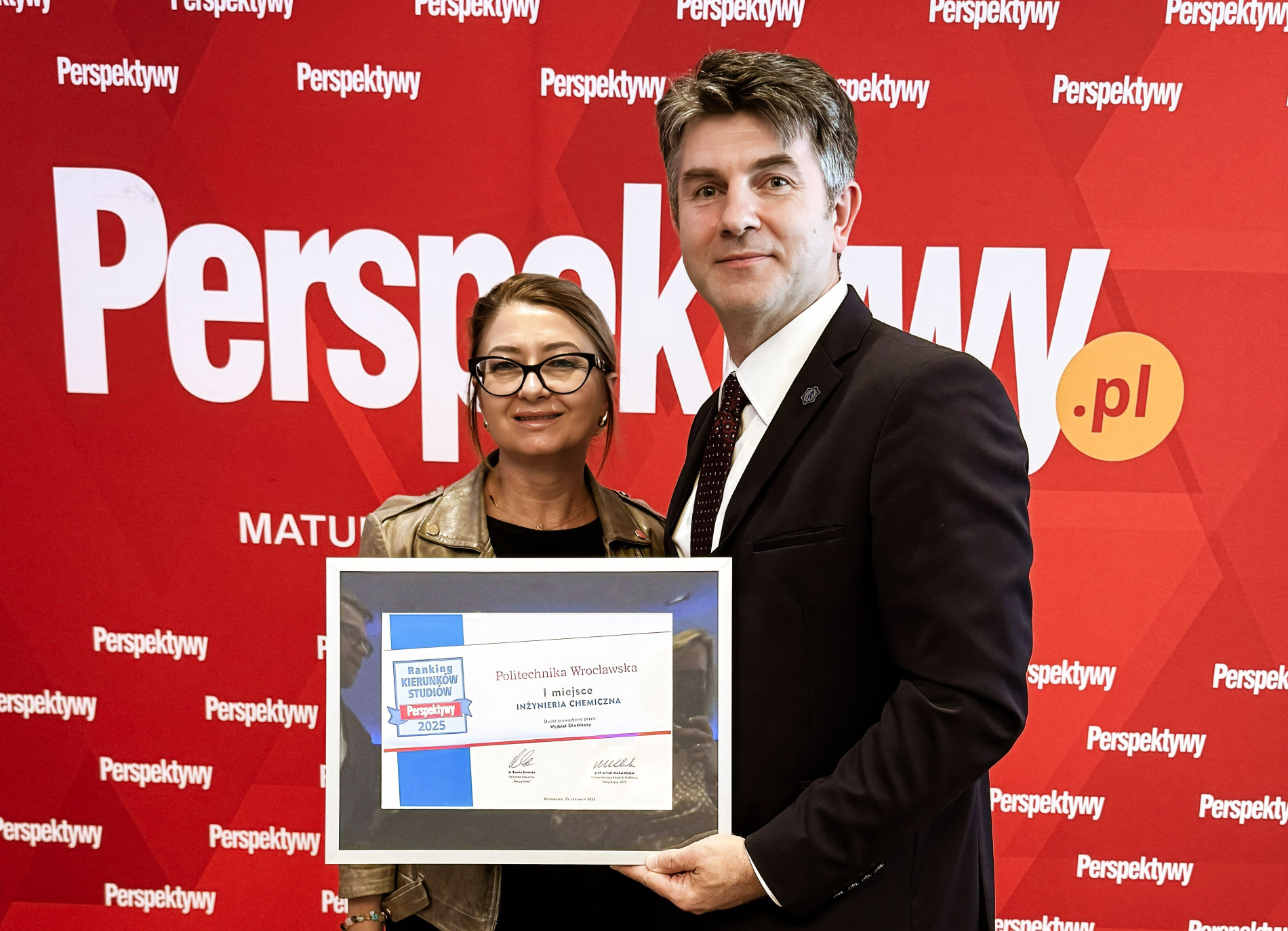 Kobieta i mężczyzna trzymają dyplom dla Politechniki Wrocławskiej za 1. miejsce w Inżynierii Chemicznej w Rankingu Kierunków Studiów Perspektywy 2025. Stoją przed ścianką z logo „Perspektywy”.
