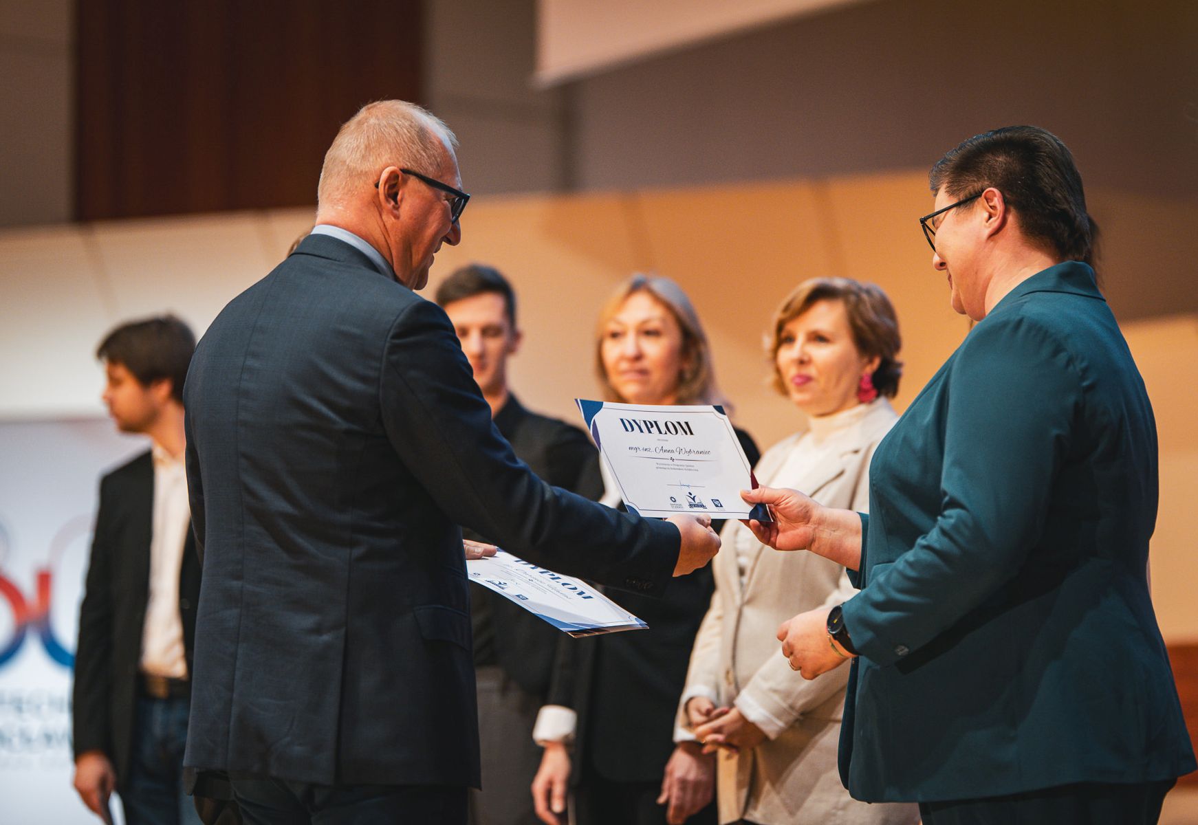Zdjęcie rektora gratulującego osobom na scenie