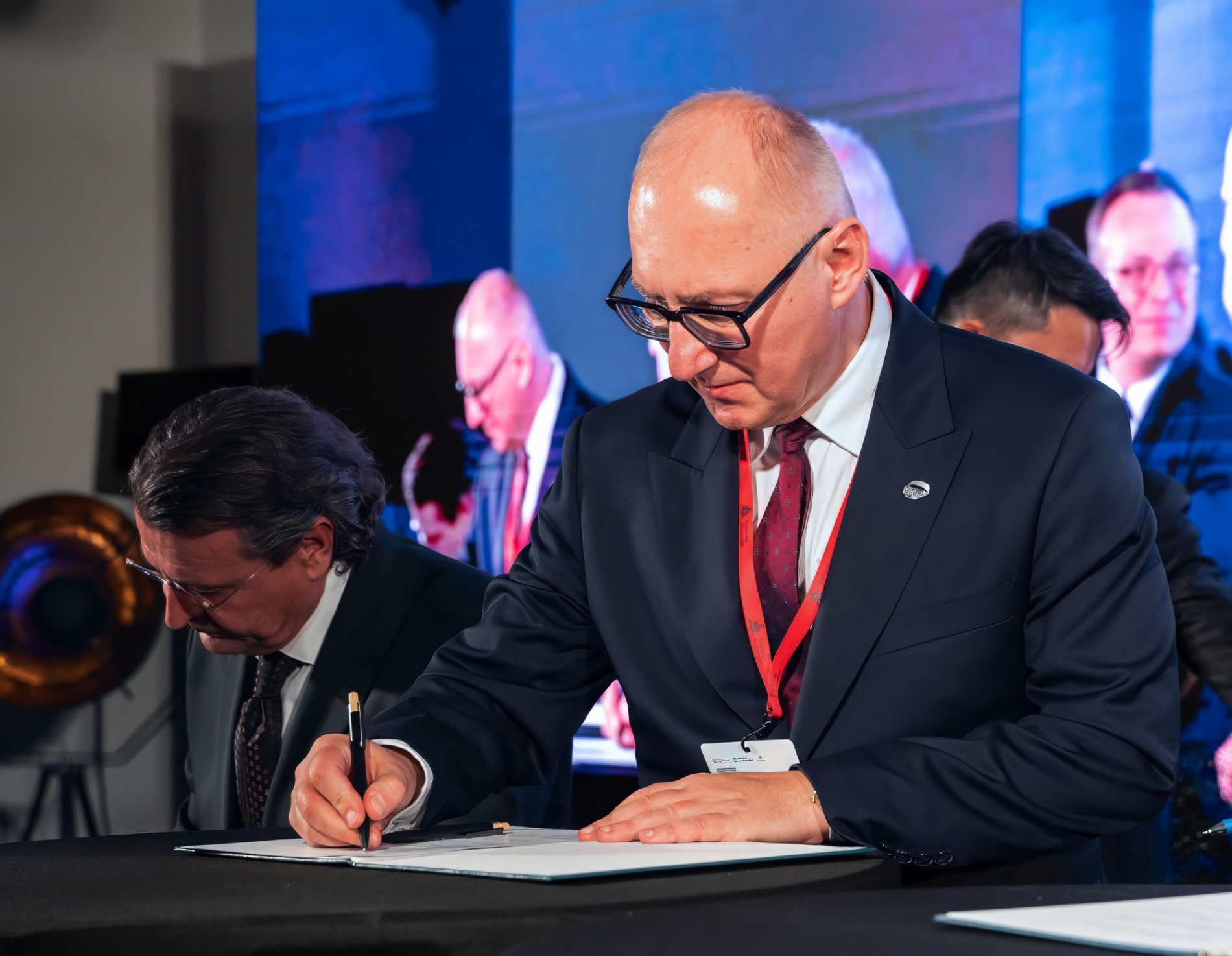 Mężczyzna w garniturze podpisuje dokument przy stole.