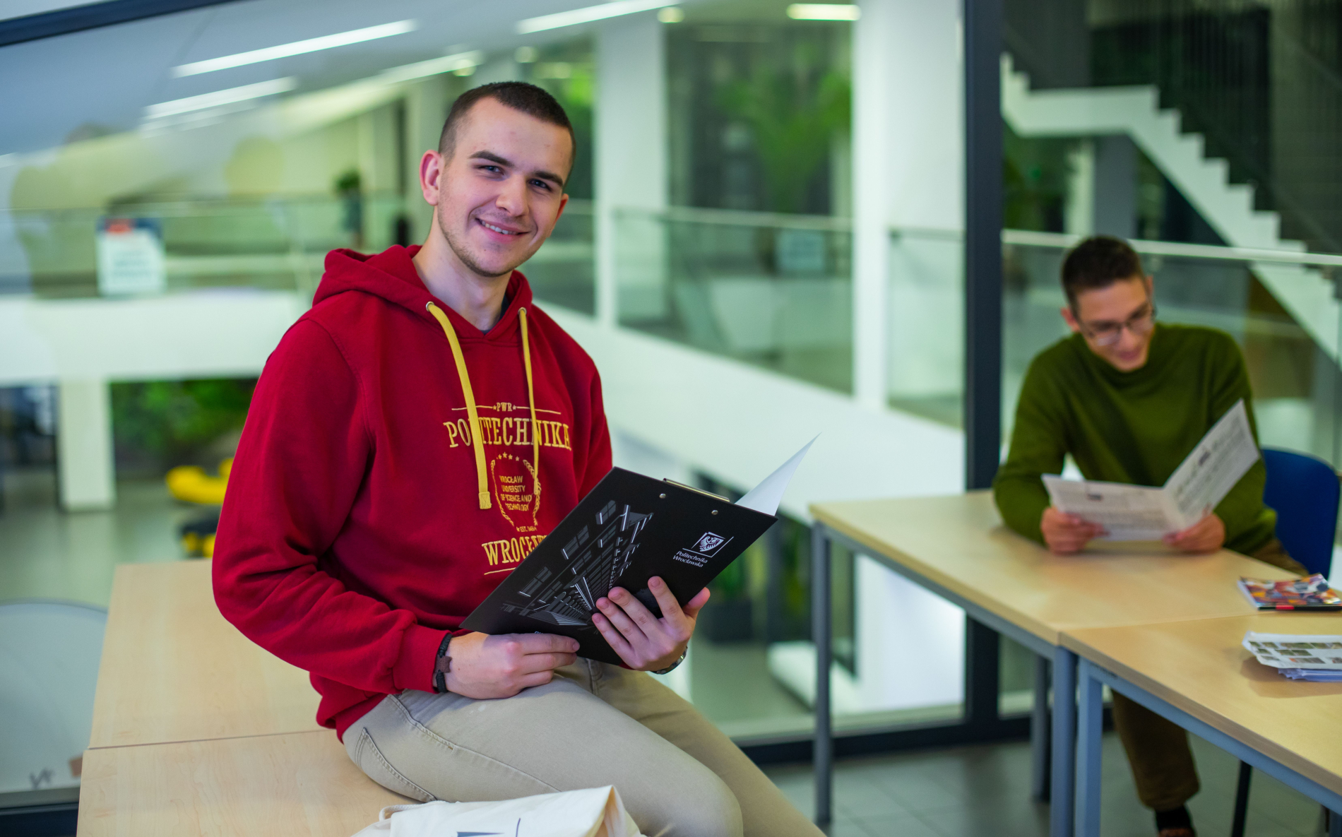 Zdjecie osoby w bluzie PWr siedzącej na ławce i trzymajacej zeszyt
