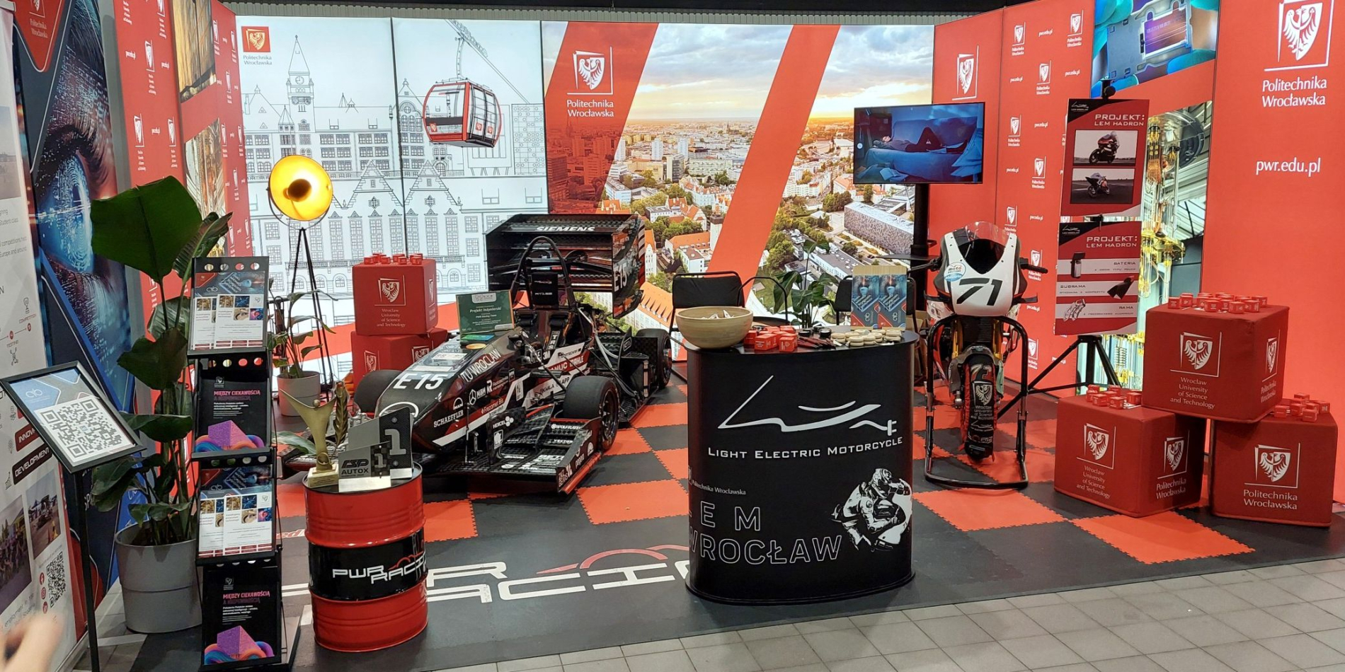 Zdjęcie stoiska PWr , na którym widać bolid i motocykl