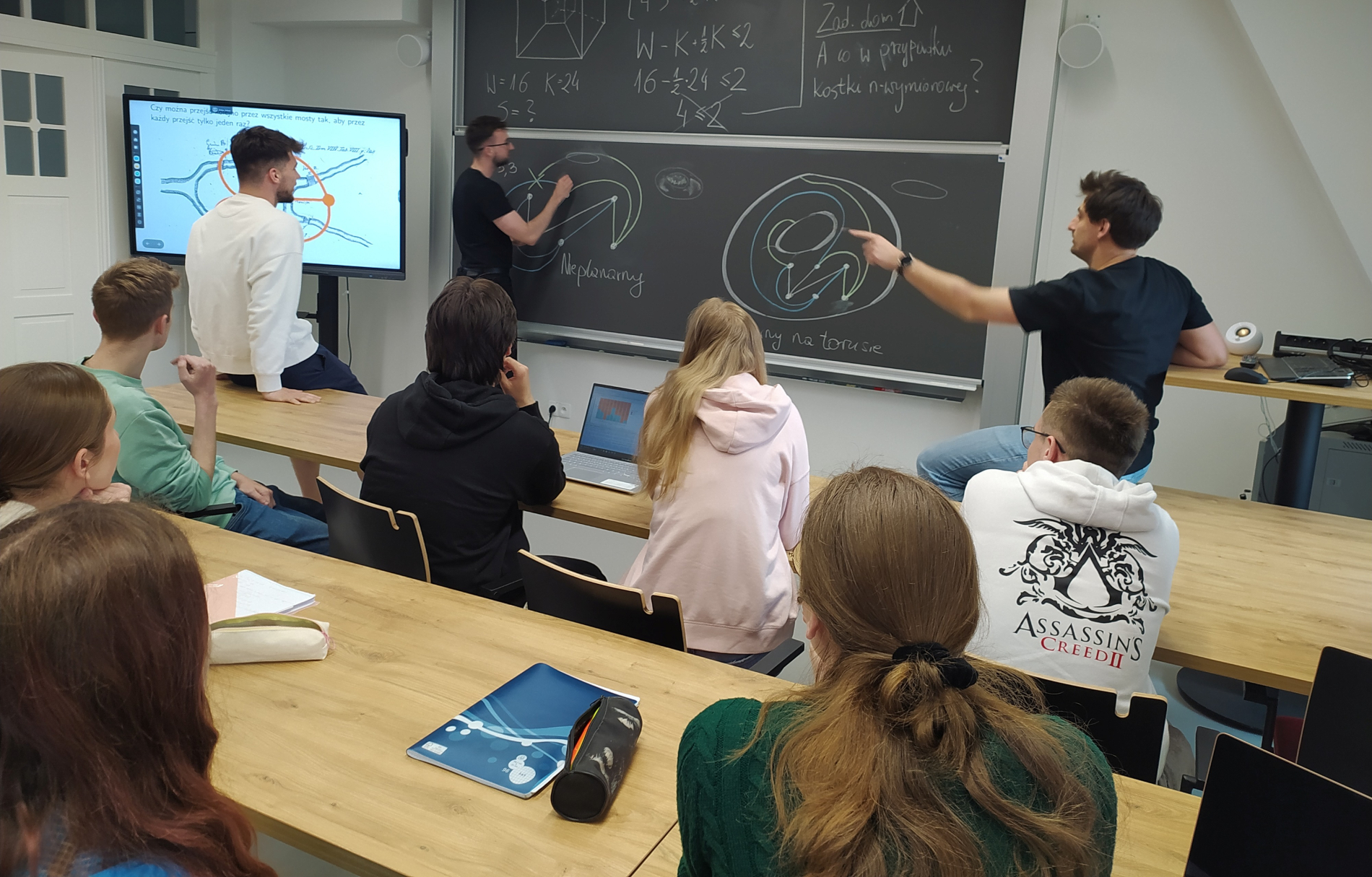 Zdjęcie osób w klasie, rozwiązujących na tablicy równania matematyczne