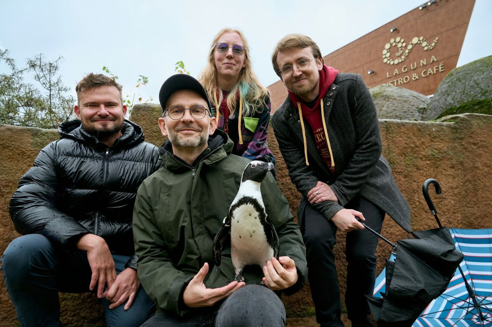 Zdjęcie grupy osób w ZOO, jedna trzyma w rękach szaroczarnego pingwina