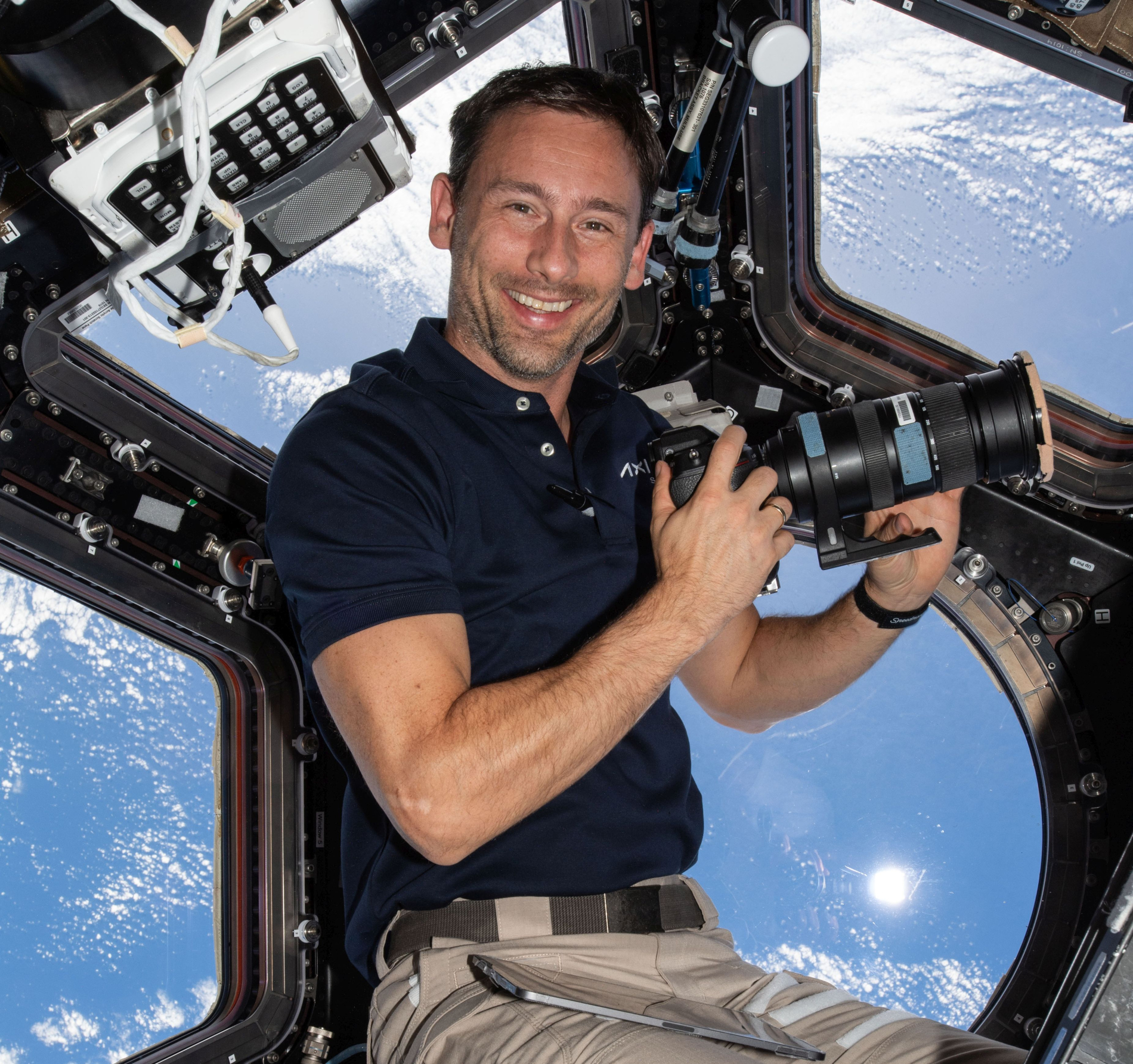 Zdjęcie uśmiechniętego człowieka z aparatem w rakiecie w tle ziemia.