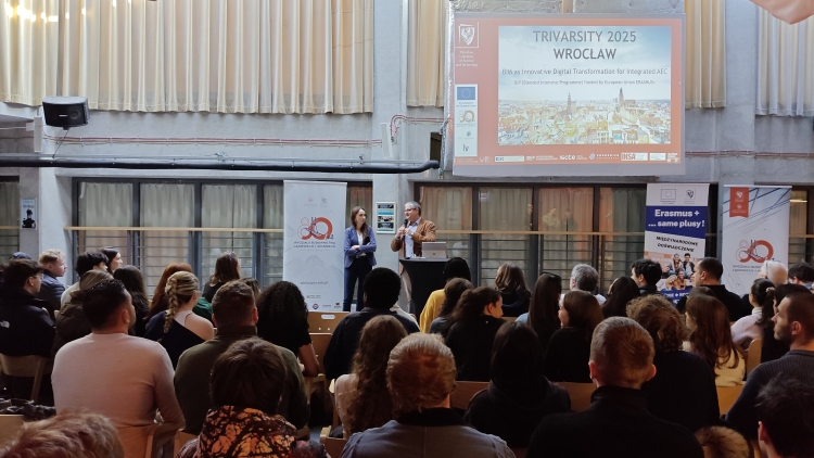 Otwarcie warsztatów projektu Trivarsity 2025. Dwoje prelegentów przed dużą widownią.