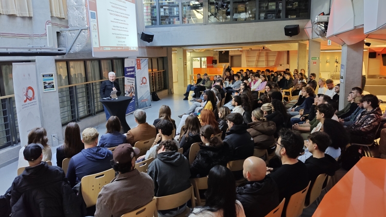 Prelegent w czarnym golfie przemawia do grupy siedzącej w audytorium.