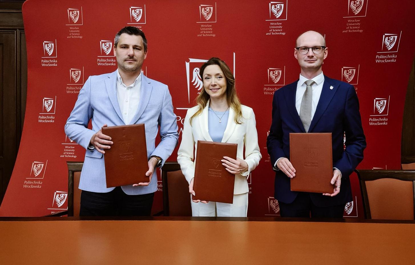 Zdjęcie trzech osób trzymających dyplomy na tle ścianki PWr