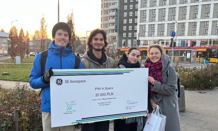 Czworo uśmiechniętych studentów pozuje z czekiem od GE Aerospace wartości 30 000 zł w otoczeniu miejskim.