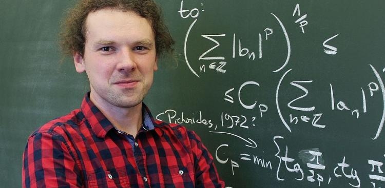 Zdjęcie dr. Kwaśnickiego stojącego na tle tablicy z wzorami matematycznymi