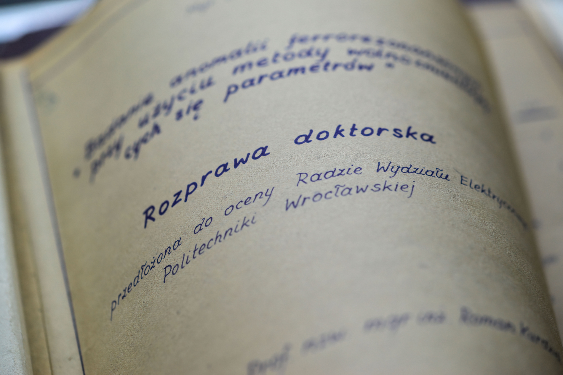 Zbliżenie na stronę starej pracy dyplomowej z niebieskim napisem: „Rozprawa doktorska, przedłożona do oceny Radzie Wydziału Elektrycznego Politechniki Wrocławskiej”.