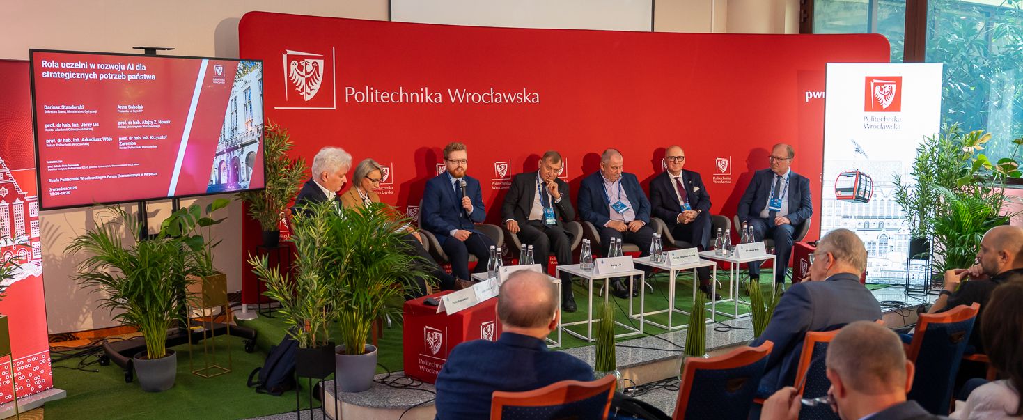 Uczestnicy panelu dyskusyjnego, w tym przedstawiciele Politechniki Wrocławskiej, siedzą na scenie przed czerwonym tłem z logo uczelni. Tłum słuchaczy obserwuje dyskusję, a na ekranie widoczny jest tytuł debaty "Rola uczelni w rozwoju AI dla strategicznych potrzeb państwa".