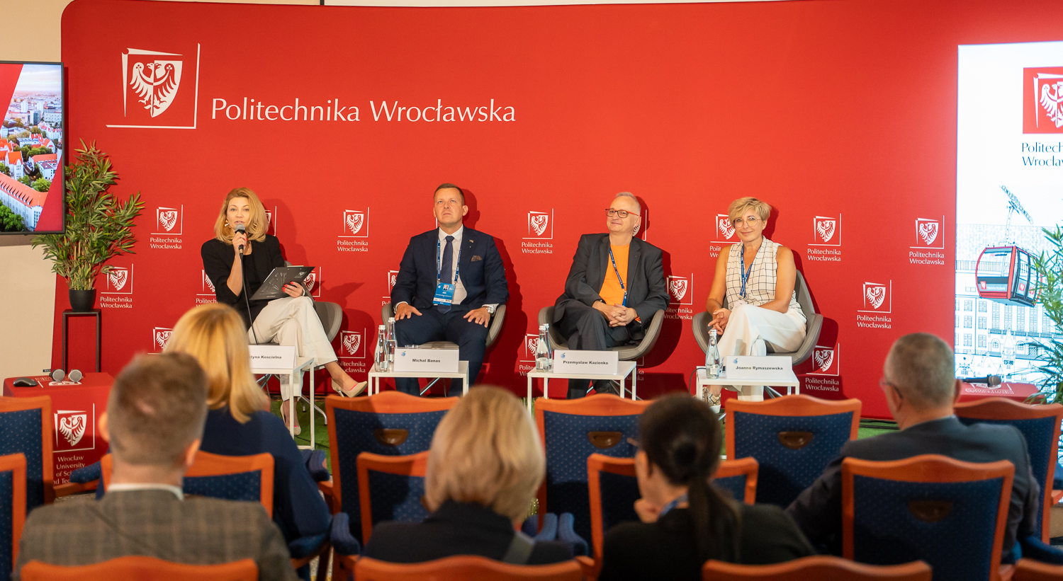 Czworo panelistów siedzi na tle czerwonej ścianki z napisem Politechnika Wrocławska.