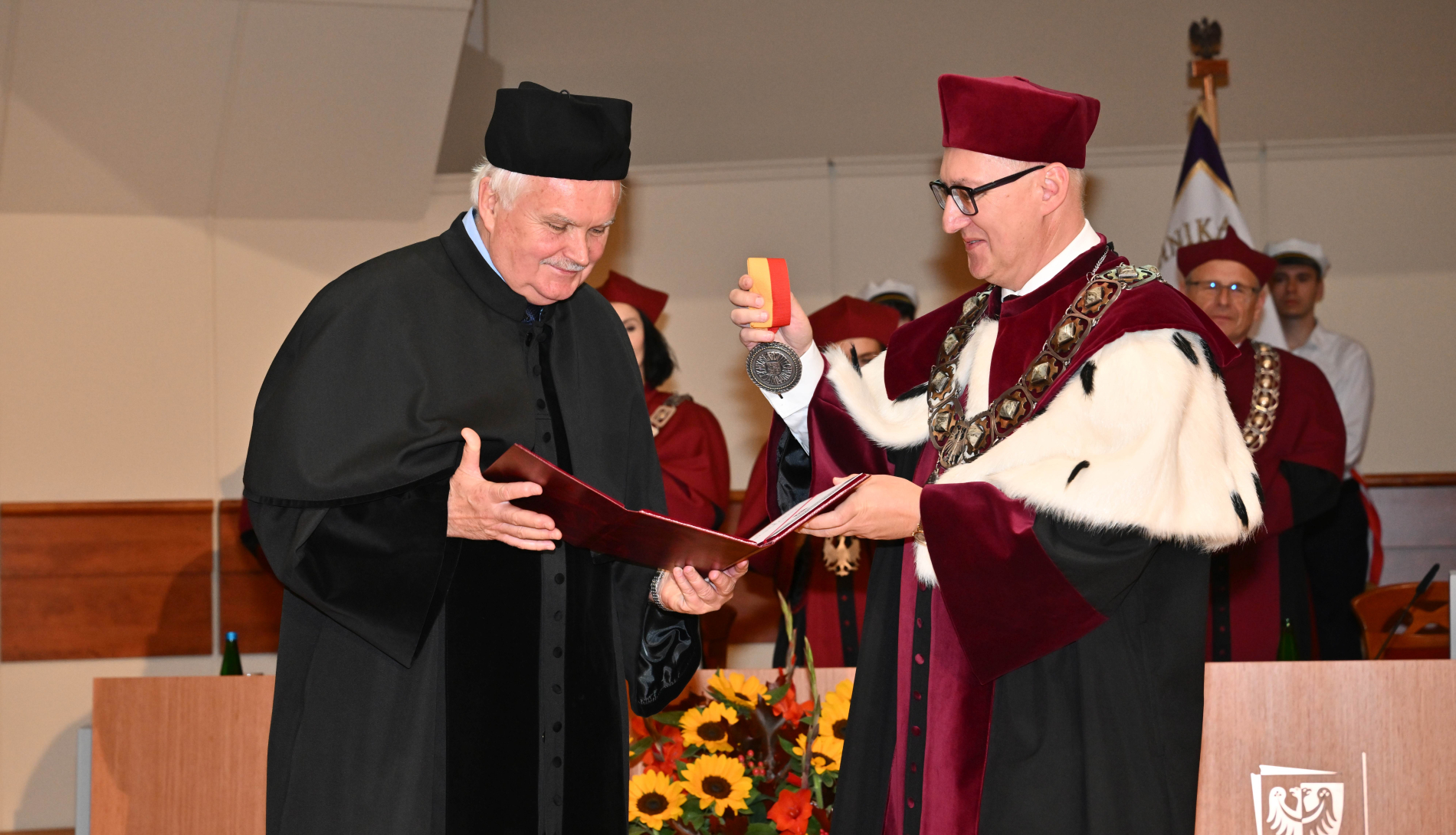 Zdjęcie osoby odbierającej medal i rektora na scenie w auli PWr