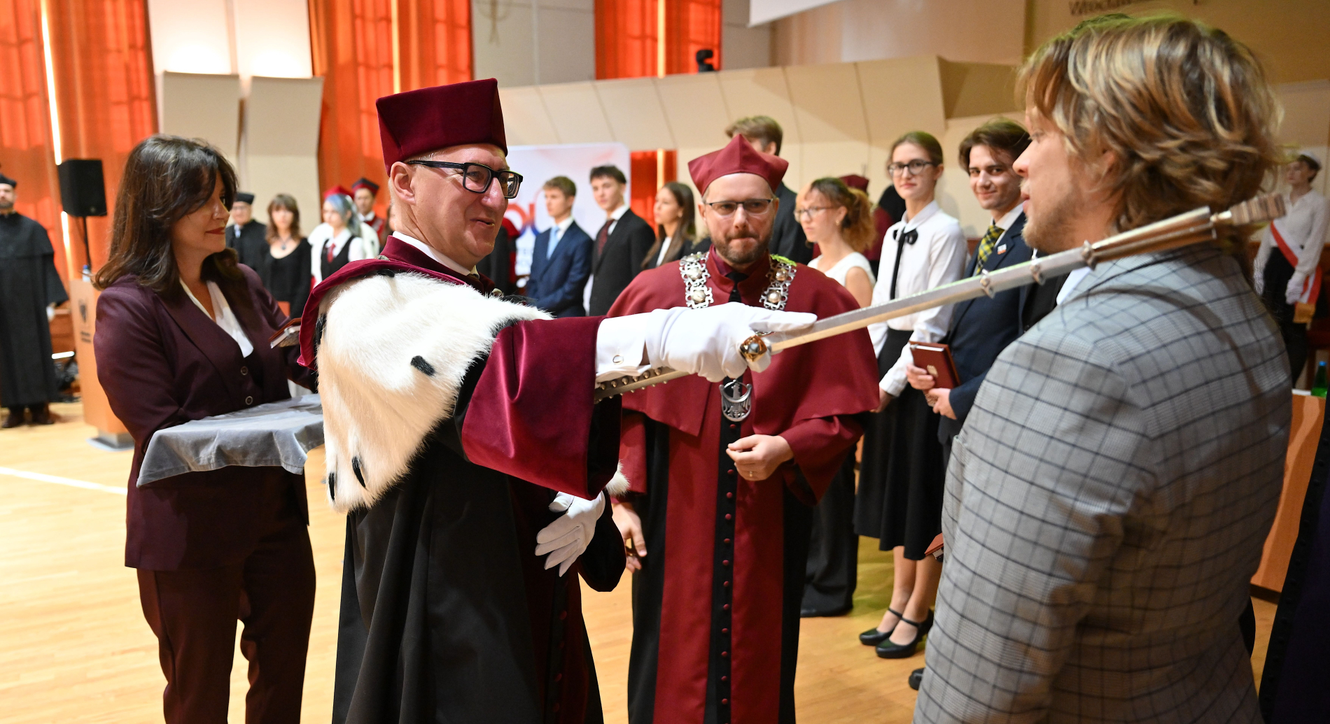 Mężczyzna w stroju rektora przeprowadza ślubowanie studentów.