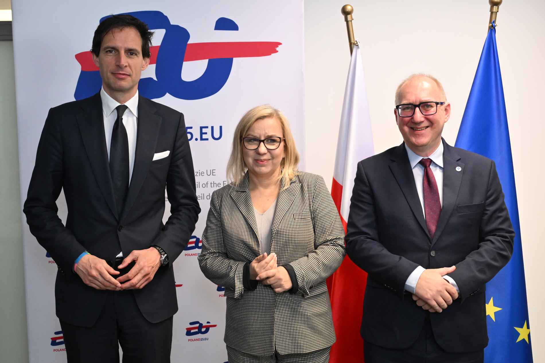 Zdjęcie trzech osób stojących obok siebie na tle flagi polski i Unii Europejskiej