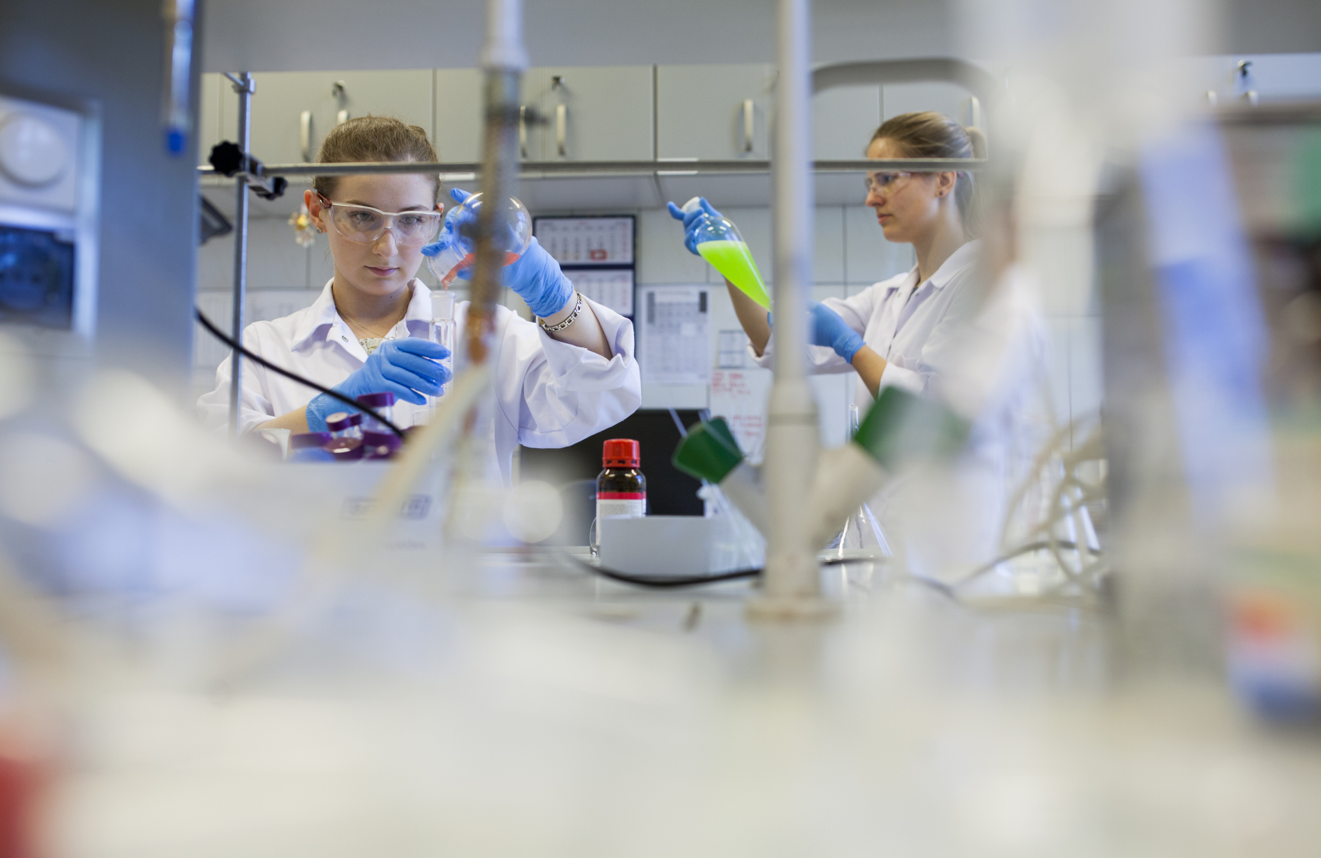 Dwie kobiety w fartuchach i okularach ochronnych pracują w laboratorium.