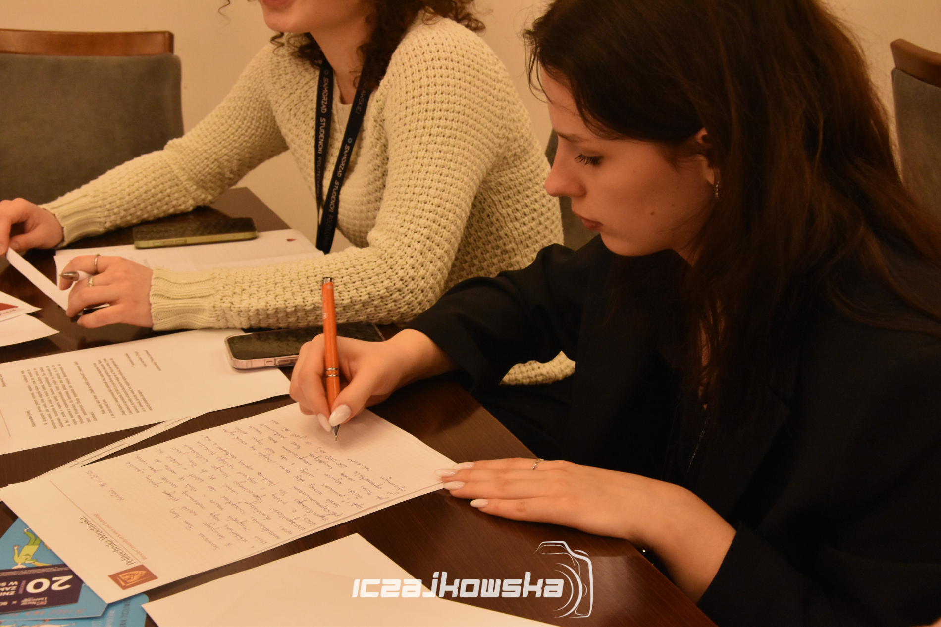 Zbliżenie na dwie młode kobiety siedzące przy stole i piszące listy.