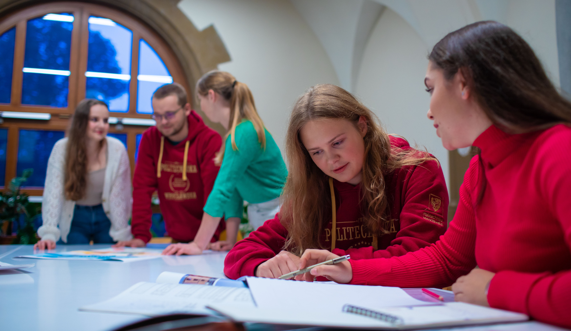 Grupa młodych ludzi siedzi przy stole i pracuje nad projektem