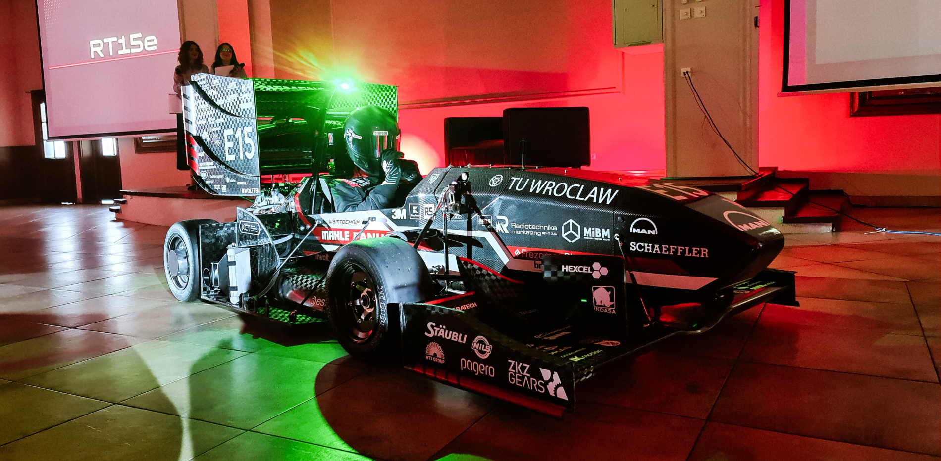 Czarny bolid wyścigowy typu Formuła Student z oznaczeniami "TU WROCŁAW" i logotypami sponsorów