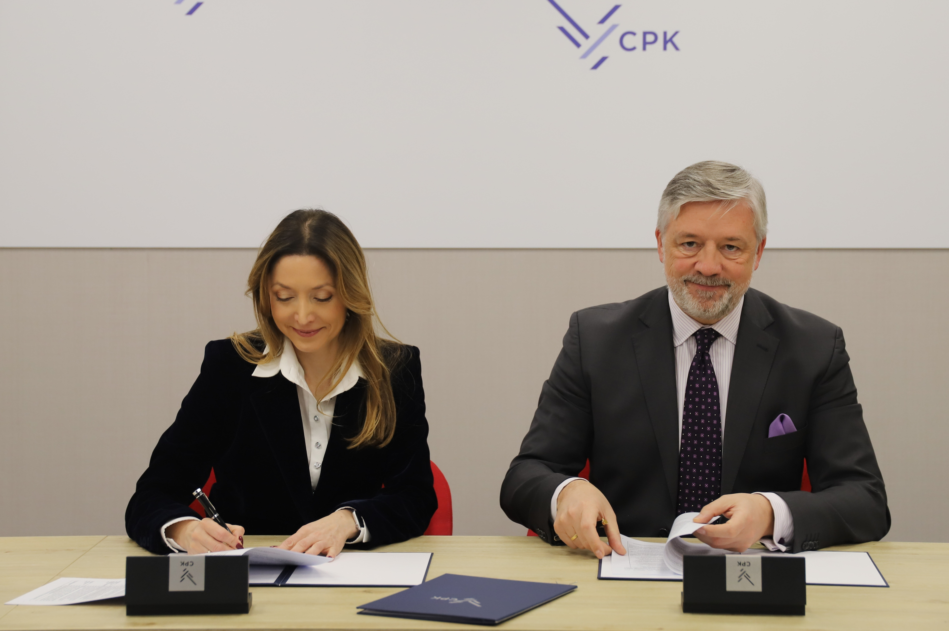 Podpisanie umowy w biurze CPK. Kobieta i mężczyzna w strojach formalnych podpisują dokumenty.