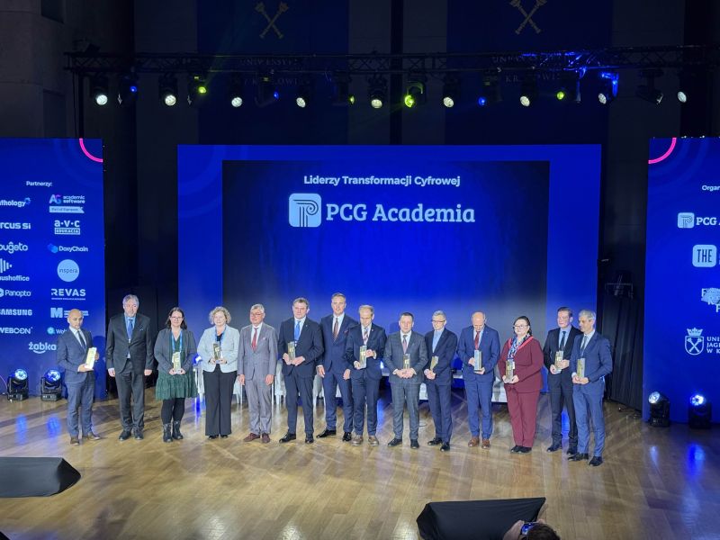 Duża grupa kilkunastu nagrodzonych osób stoi na scenie, trzymając statuetki, podczas gali PCG Academia.