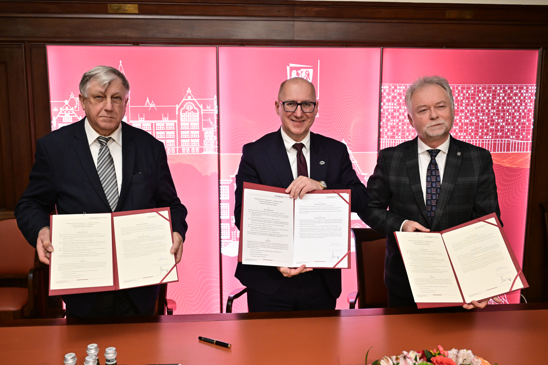 Trzej mężczyżni w garniturach prezentują podpisane umowy.