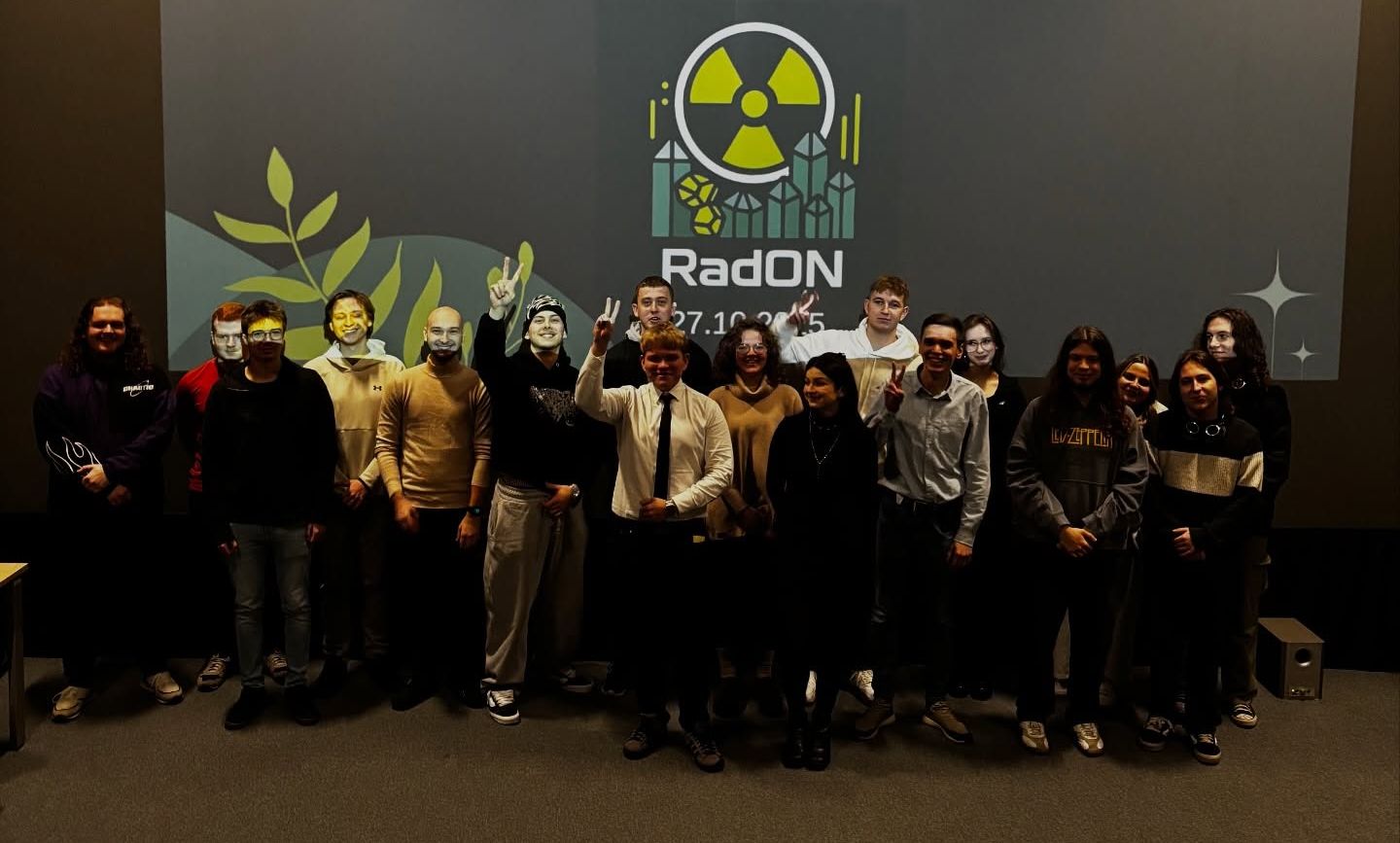 Grupa studentów i studentek pozuje w sali wykładowej. W tle na ekranie wyświetlone jest logo i nazwa konferencji lub wydarzenia "RadON".