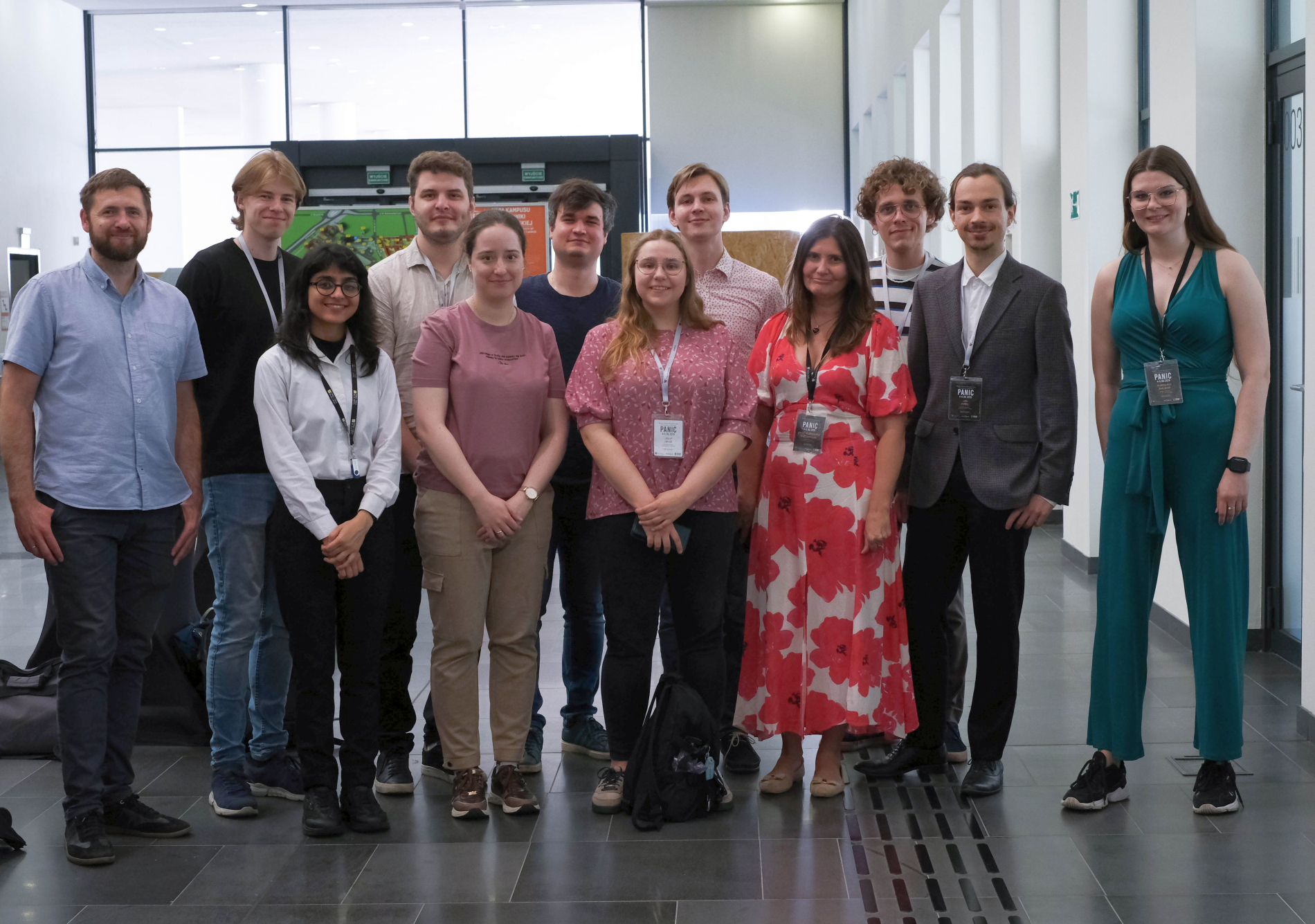 Grupa studentów w nieformalnych strojach stoi w holu nowoczesnego budynku.