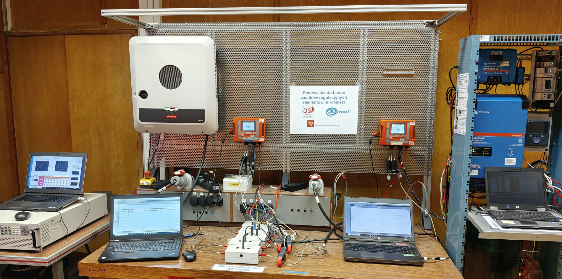 Stanowisko laboratoryjne do badań mikrosieci: na kratownicy wiszącej nad stołem widoczny jest inwerter fotowoltaiczny i mierniki.