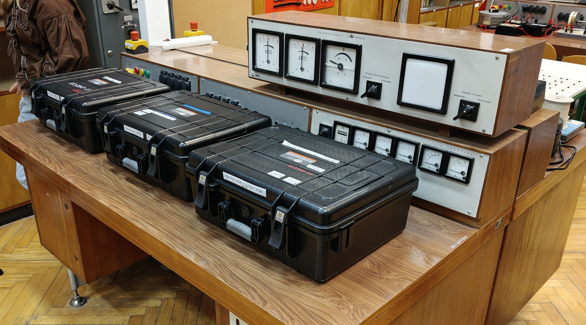 rzy czarne, prostokątne walizki leżące na drewnianym stole laboratoryjnym.