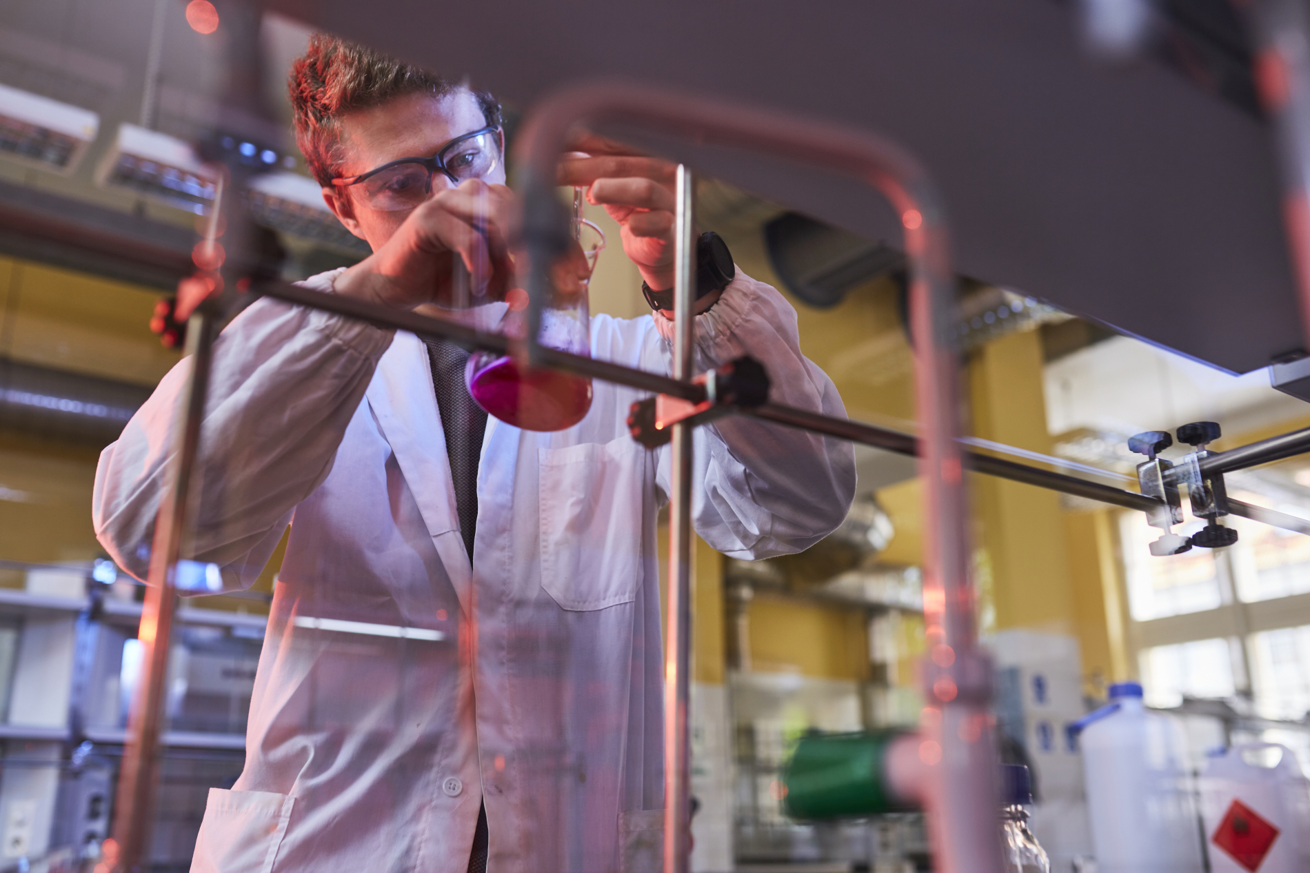 Zdjęcie osoby w laboratorium, przelewa próbkę z jednego naczynia do drugiego