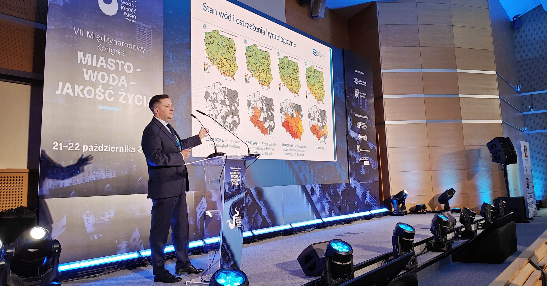 Mężczyzna w garniturze przemawia z mównicy podczas VII Międzynarodowego Kongresu "Miasto - Woda - Jakość Życia".