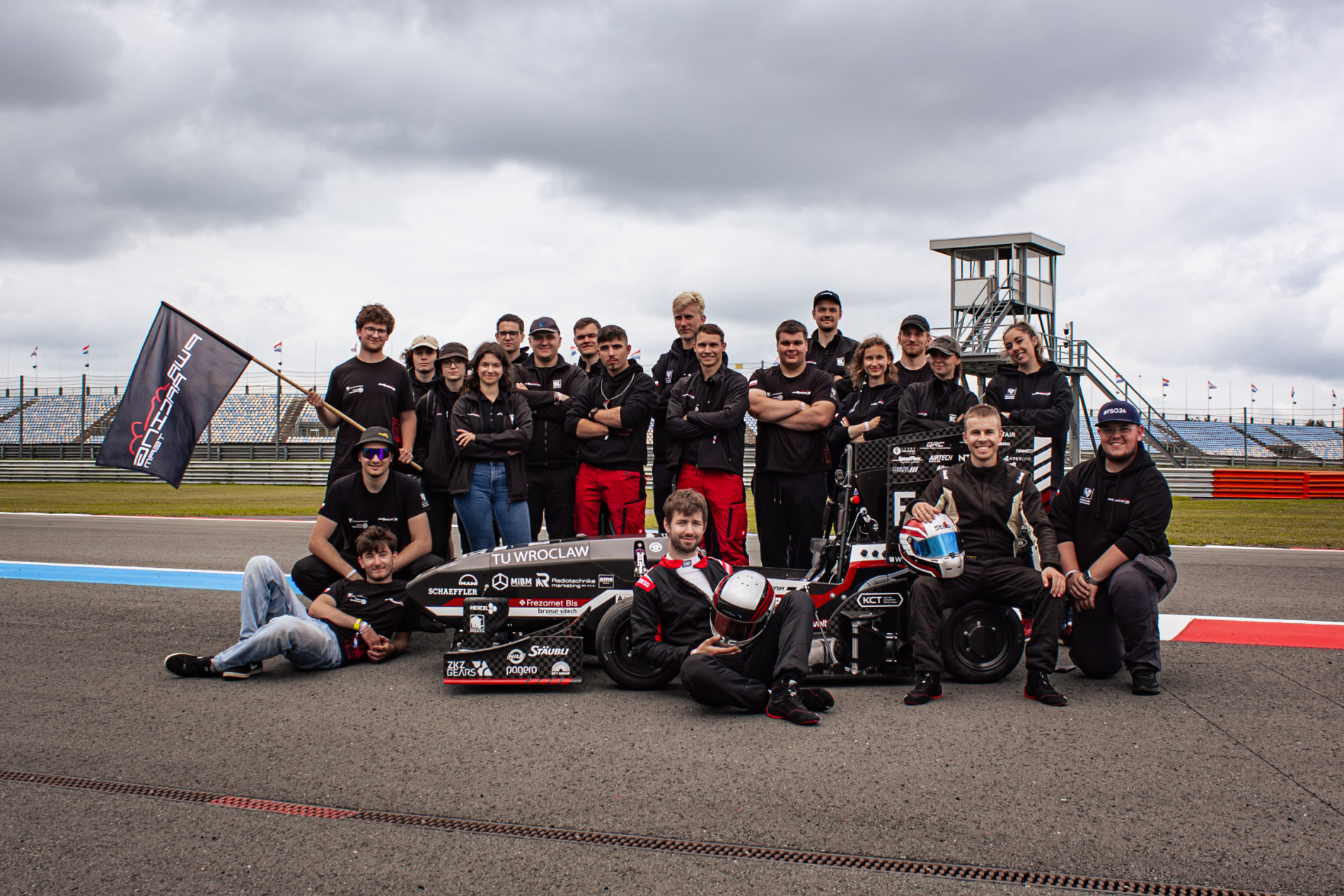 Zdjęcie zespołu pwr racing team na torze wyścigowym obok bolidu