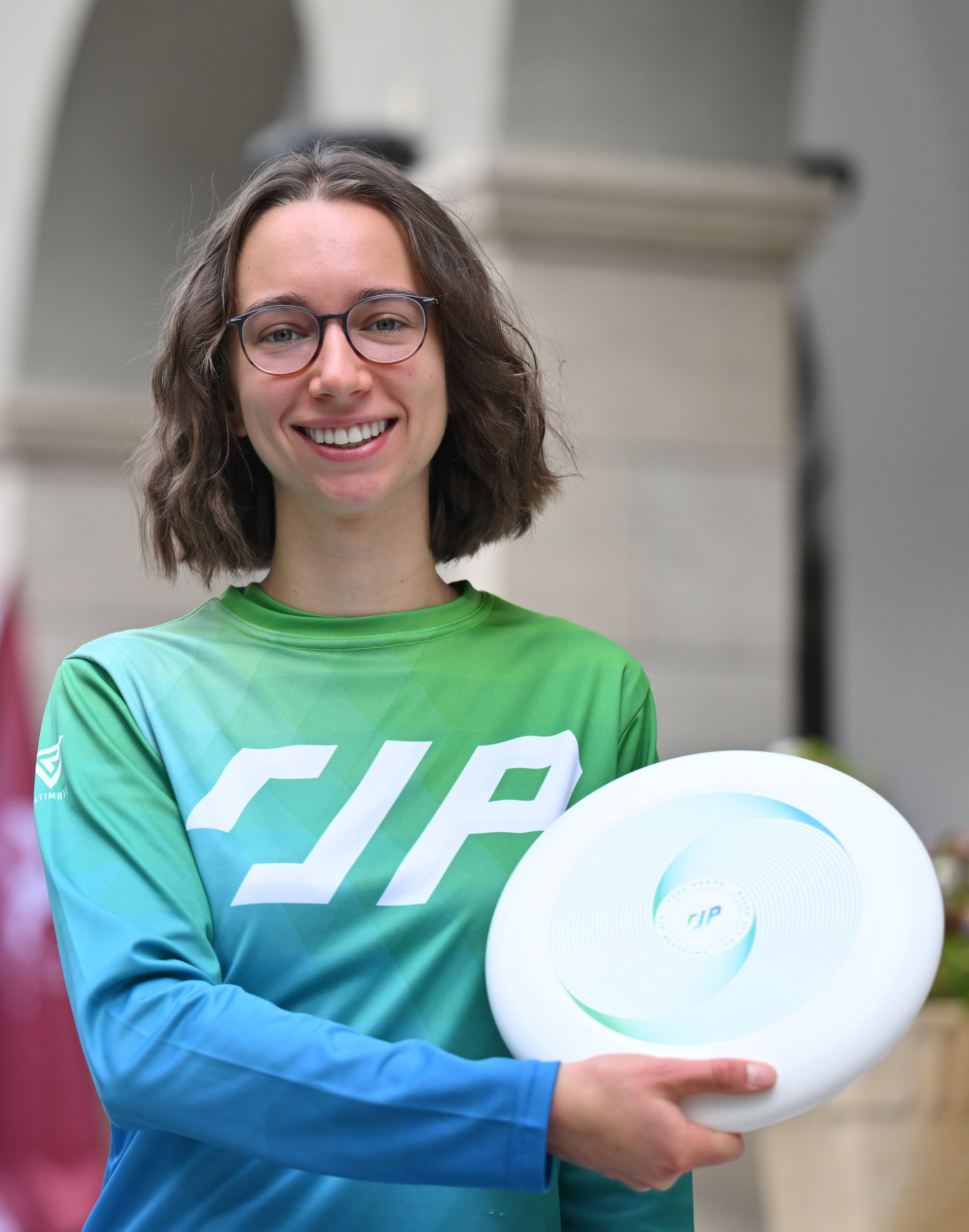 Młoda kobieta w okularach, klubowej bluzie, trzyma białe frisbee