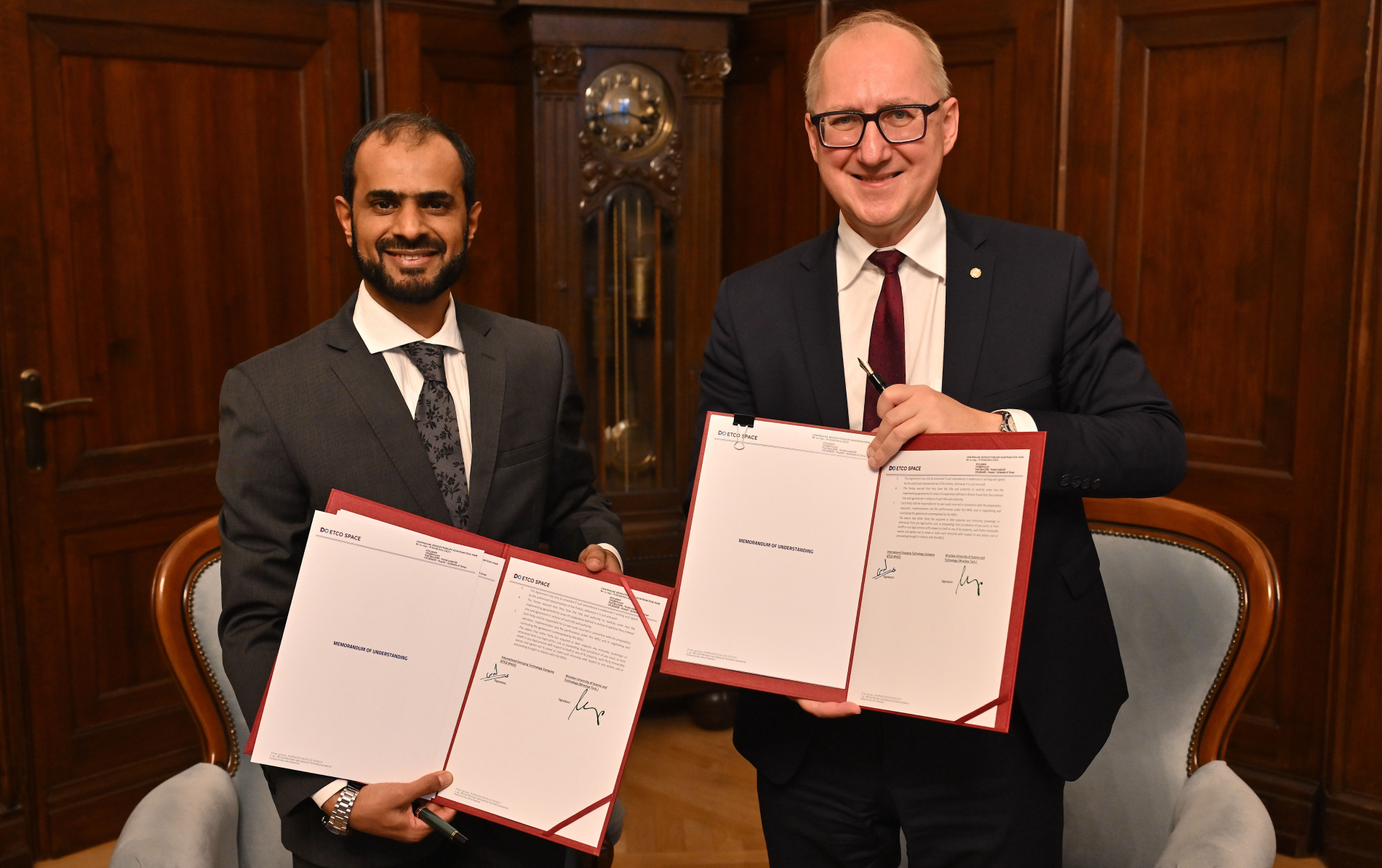 Two men in suits hold signed documents.