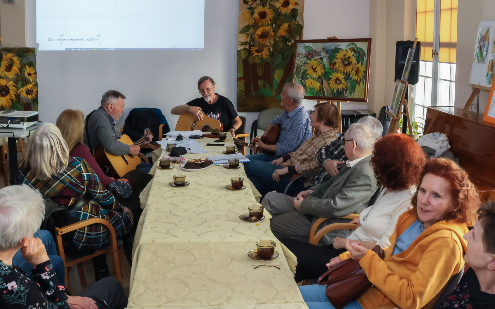 Osoby siedziące przy stole, śpiewające, jedna trzyma gitarę